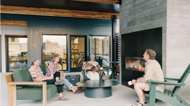 Modern outdoor patio with mixed seating, wood beams, and a concrete fireplace under a covered roof structure