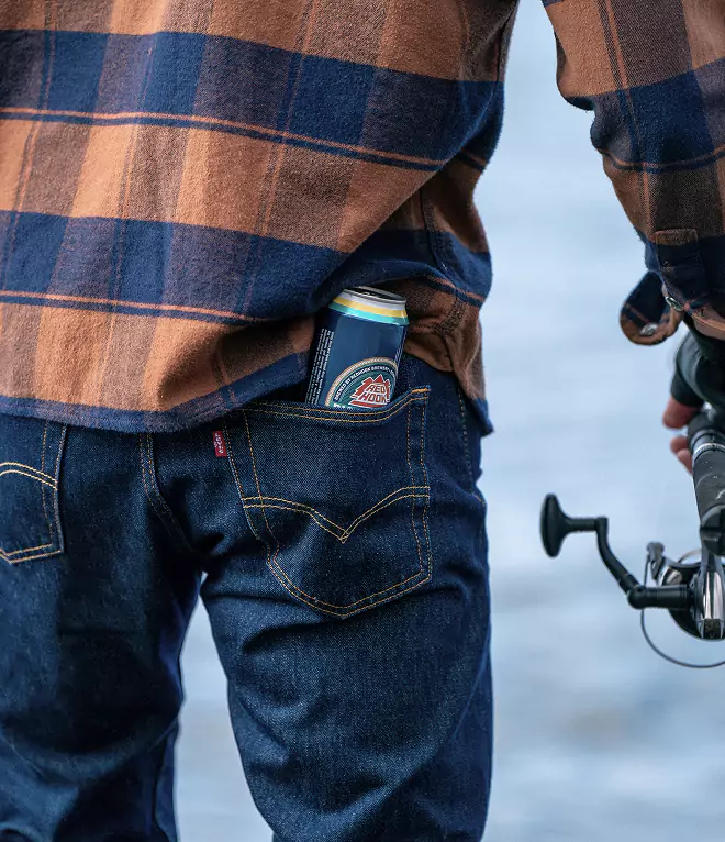 Close-up of a back pocket holding a Redhook Brewery beer can, with a fishing reel visible in hand.