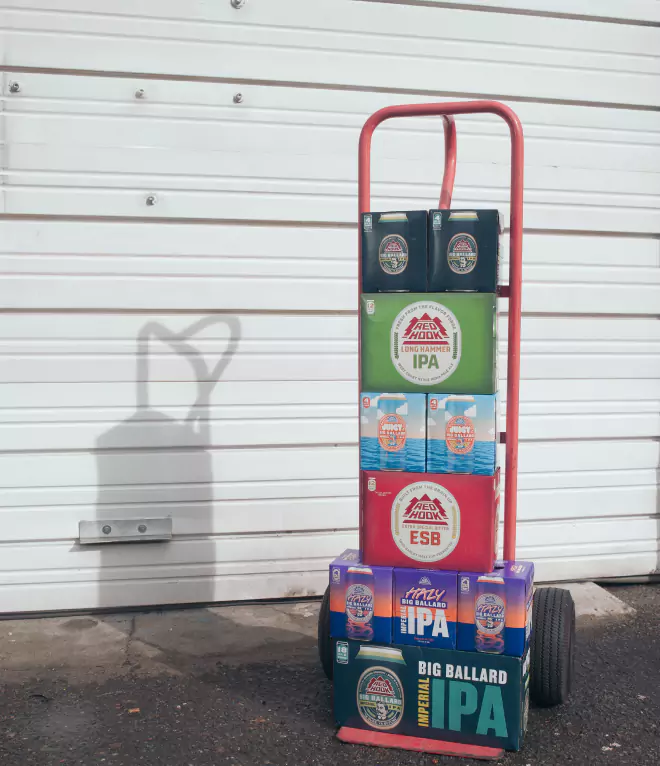 Hand truck stacked with various Redhook Brewery beer packs, positioned against a white industrial wall.